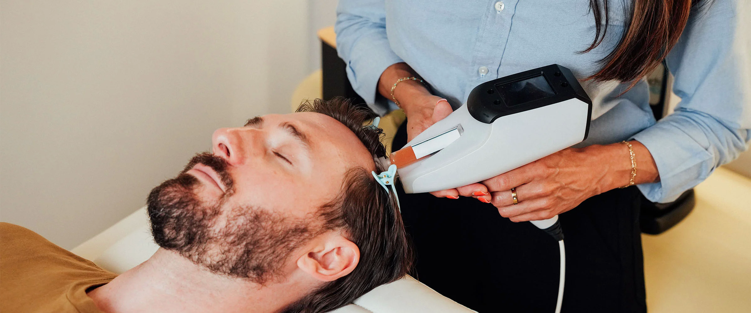 Provider using a CryoWave CX handheld device to treat a reclining man’s scalp.