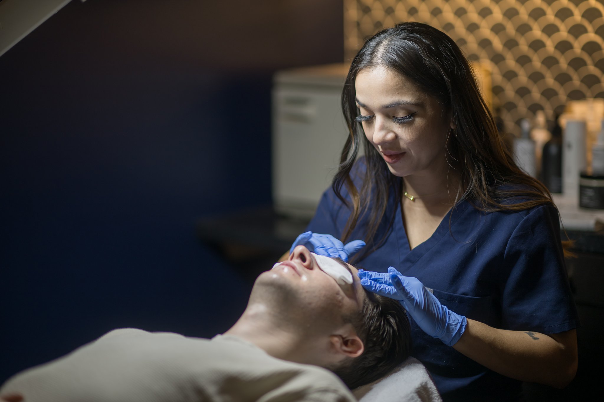 Aurora/Esthetician applying a chemical facial peel to a male client with protective pads covering his eyes at Flycatcher in Austin.